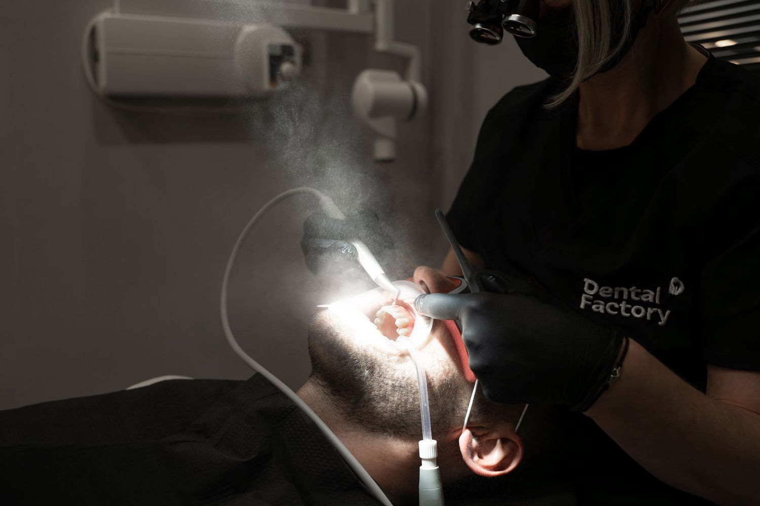 Closeup of dental procedure showing illuminated dental tools and steam in dark setting.