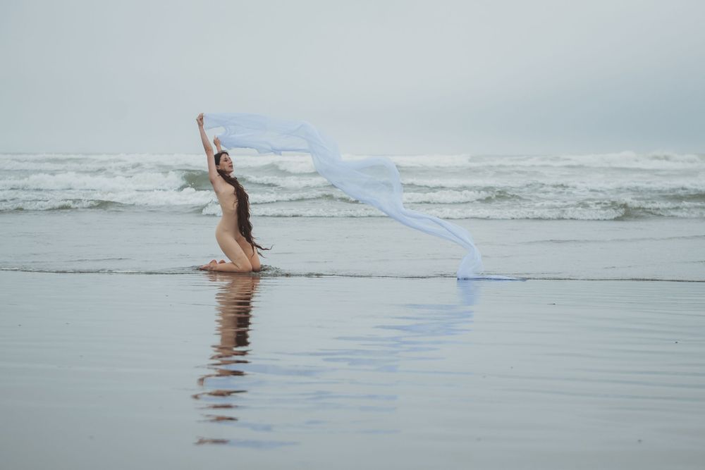 A figure dances on a reflective beach with a flowing blue ribbon creating graceful patterns in the air.
