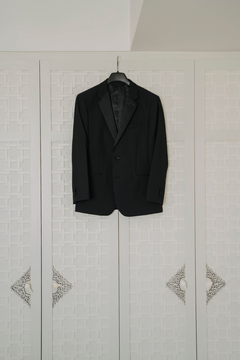Black suit jackets hanging on white closet doors with decorative trim details.
