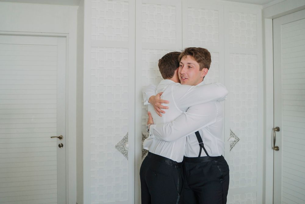 Two people in white formal attire embracing in a bright indoor setting.