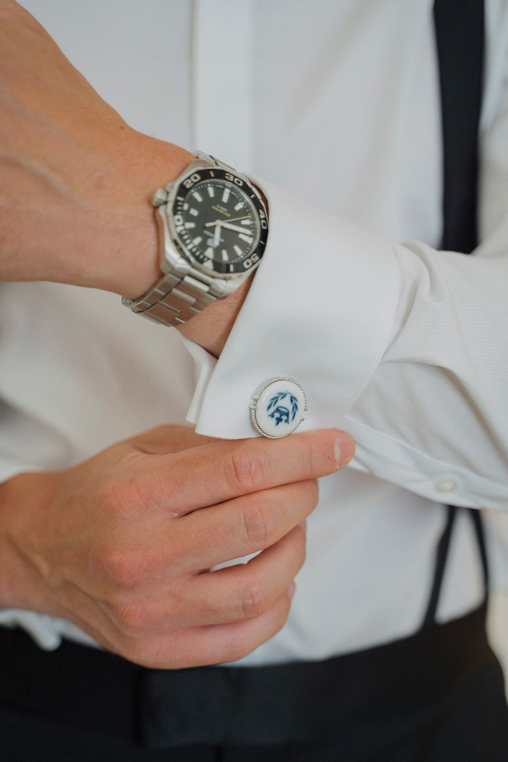 Close-up of luxury watch and cufflinks being adjusted on formal white shirt sleeve.