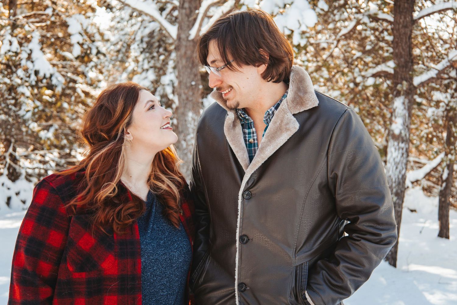 A couple shares a joyful moment together in a snowy winter scene wearing plaid and gray coats.