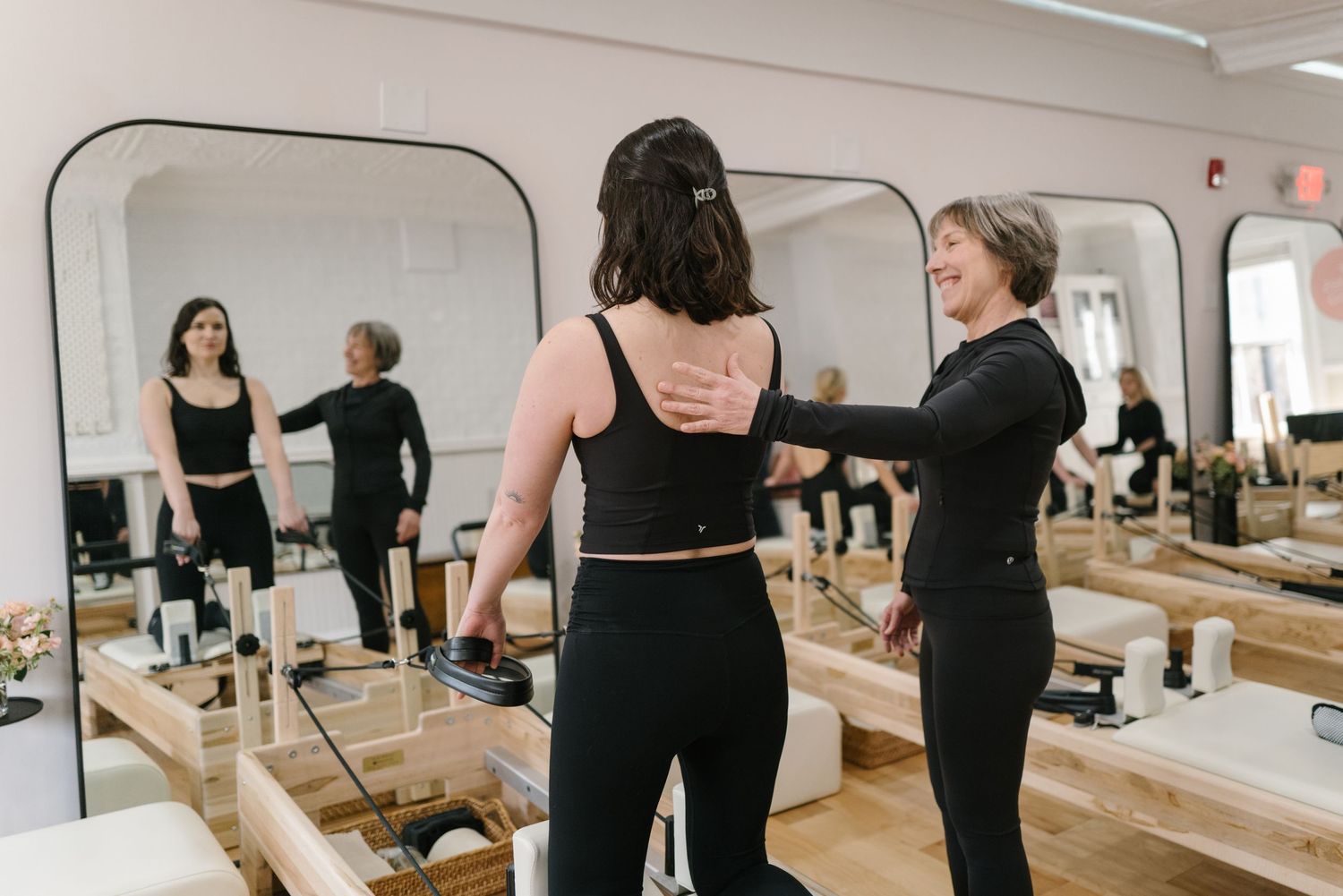 A group of dancers in black attire smile together while taking a mirror selfie in a dance studio.