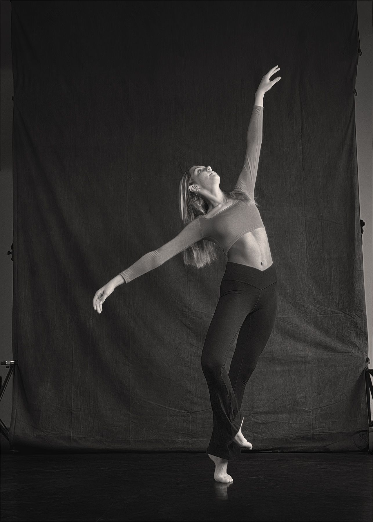 A dancer performs an expressive contemporary dance pose against a dark backdrop in black and white photography.