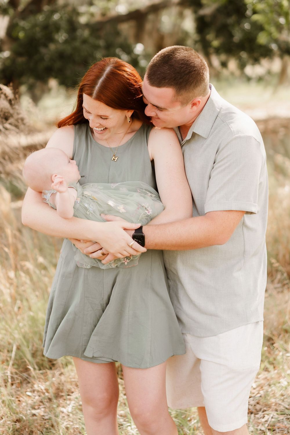 A couple in sage green and white outfits share tender moments together in a sunlit outdoor setting.