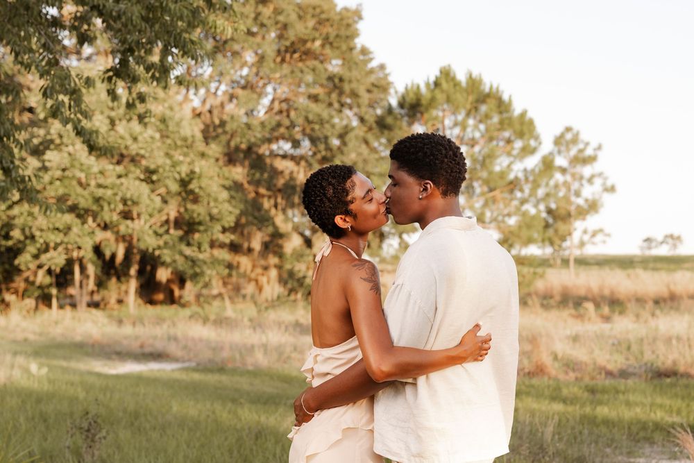 A romantic couple embraces in a golden field during sunset while wearing white outfits for their engagement photos.
