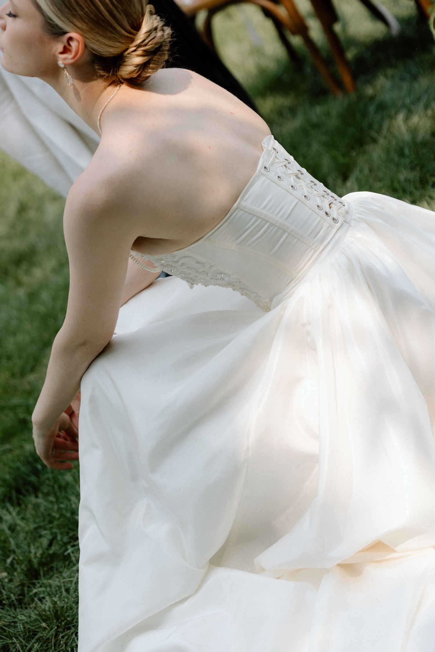 Elegant wedding dress displayed against white draped backdrop with floral arrangements and greenery on grass.