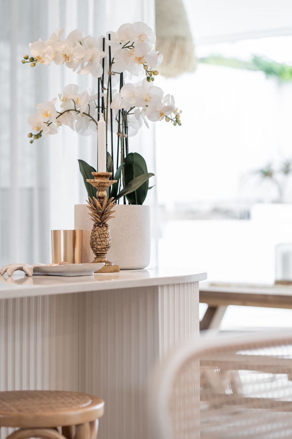 White orchid centerpieces on fluted pedestal tables create an elegant dining room display with natural light.