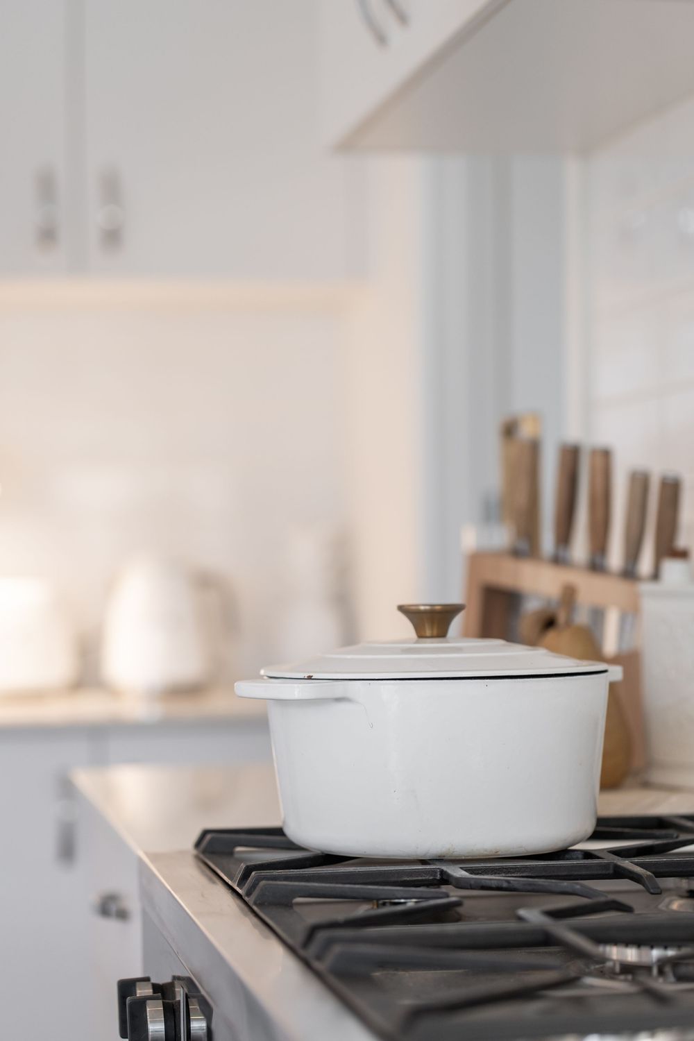 A white ceramic Dutch oven pot sits on a modern gas stovetop in a bright, minimalist kitchen.