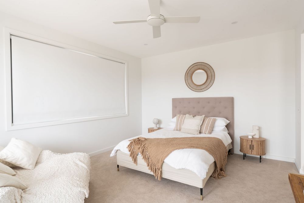 A bright, minimalist bedroom with white walls, a ceiling fan, and a cozy bed with neutral bedding.