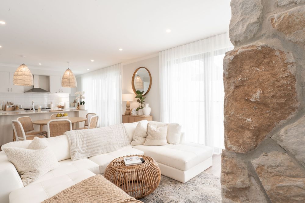 Bright coastal living room with white sectional sofa, rattan coffee table and stone accent wall in neutral tones.