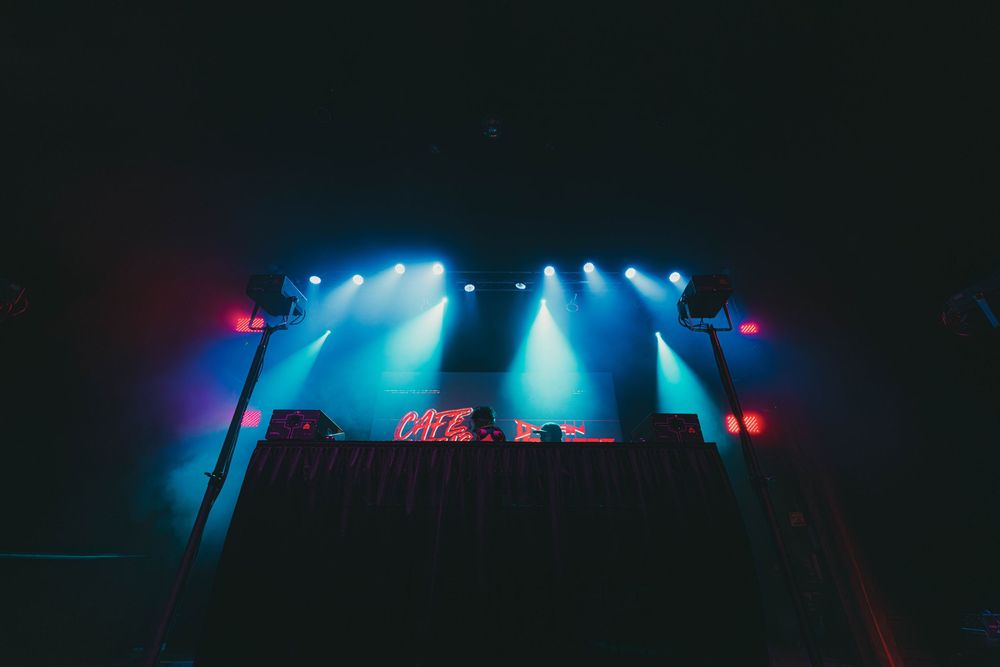 Concert stage bathed in blue and red lighting with silhouetted equipment creating a moody nighttime atmosphere.
