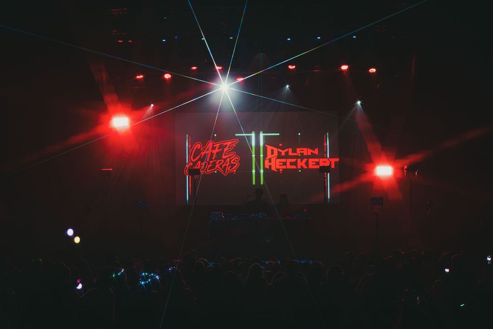 Red and white neon signs illuminate a dark stage with dramatic lighting and smoke effects.