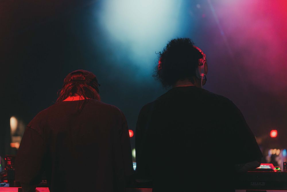 A DJ performs at a nightclub with colorful red and blue lighting creating an atmospheric ambiance.
