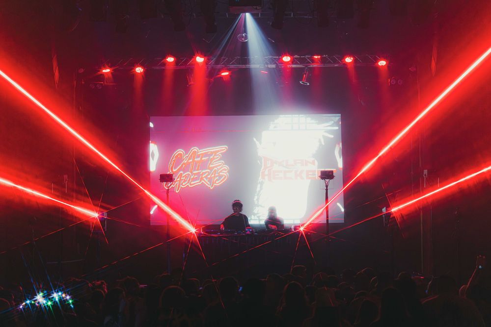 Concert stage illuminated with dramatic red laser lights and spotlights creating an energetic atmosphere during performance.