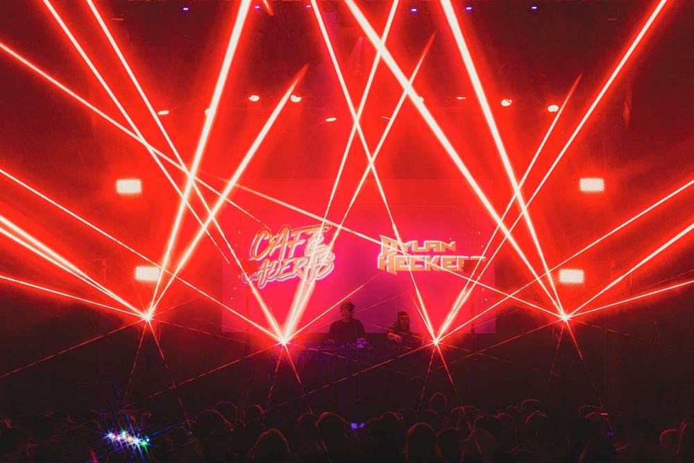 Red laser beams illuminate a dark concert venue during an energetic live performance.