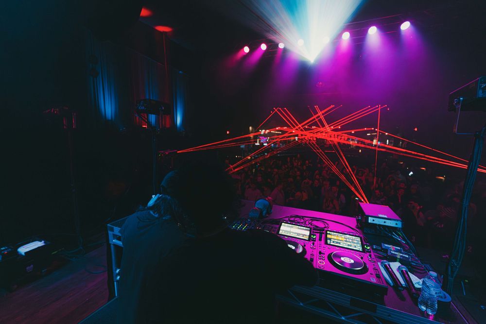 DJ performs at nightclub with vibrant purple lighting and red laser beams illuminating the dance floor.
