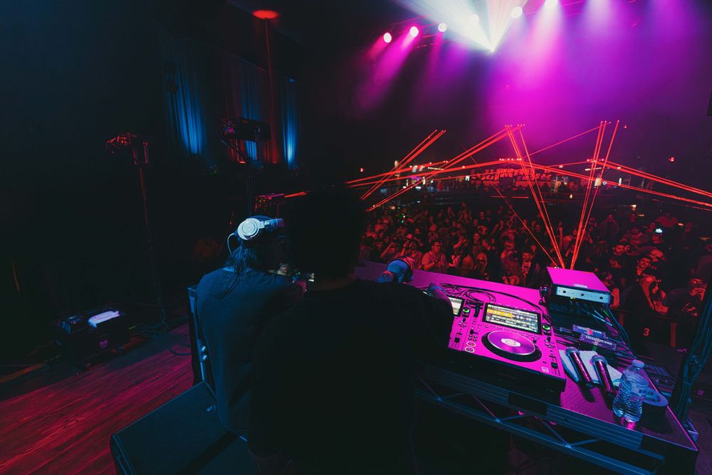 Concert venue illuminated with vibrant pink and blue lights during a live performance with crowd silhouettes visible.
