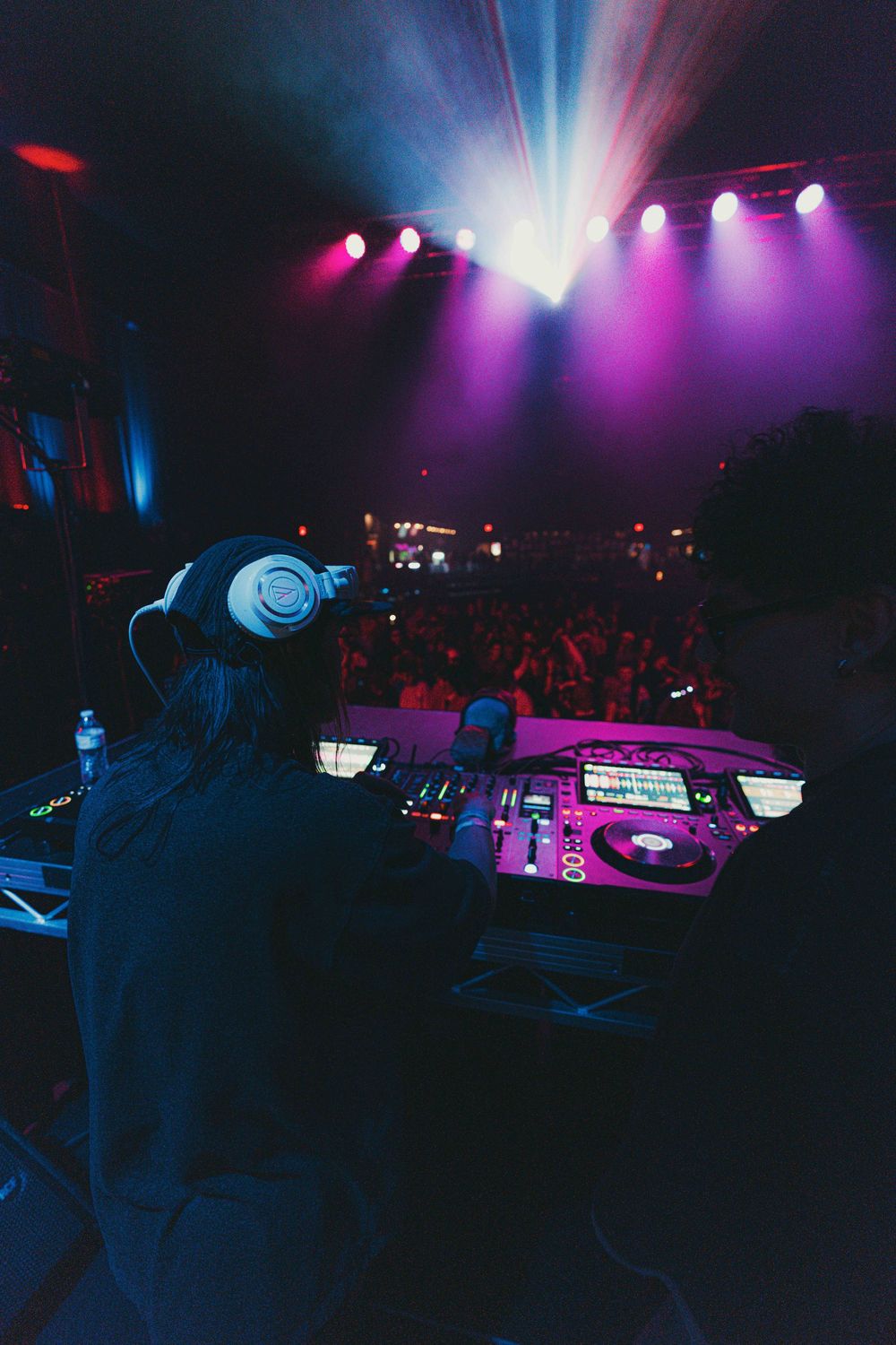 DJ performs at nightclub with colorful purple and blue lighting illuminating the dark dance floor and stage setup.