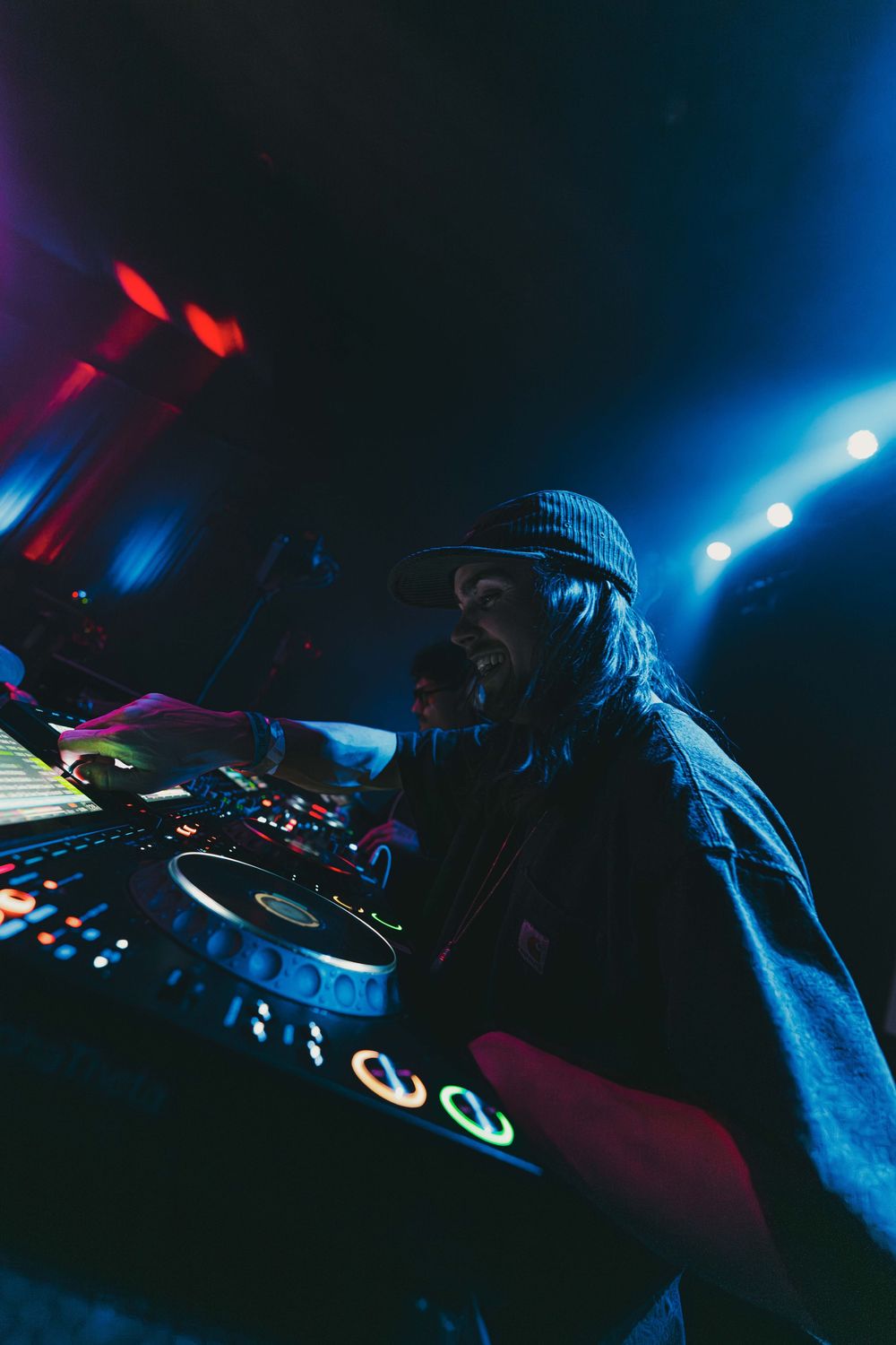 DJ performing at night with blue lighting and electronic equipment creating an atmospheric club environment.