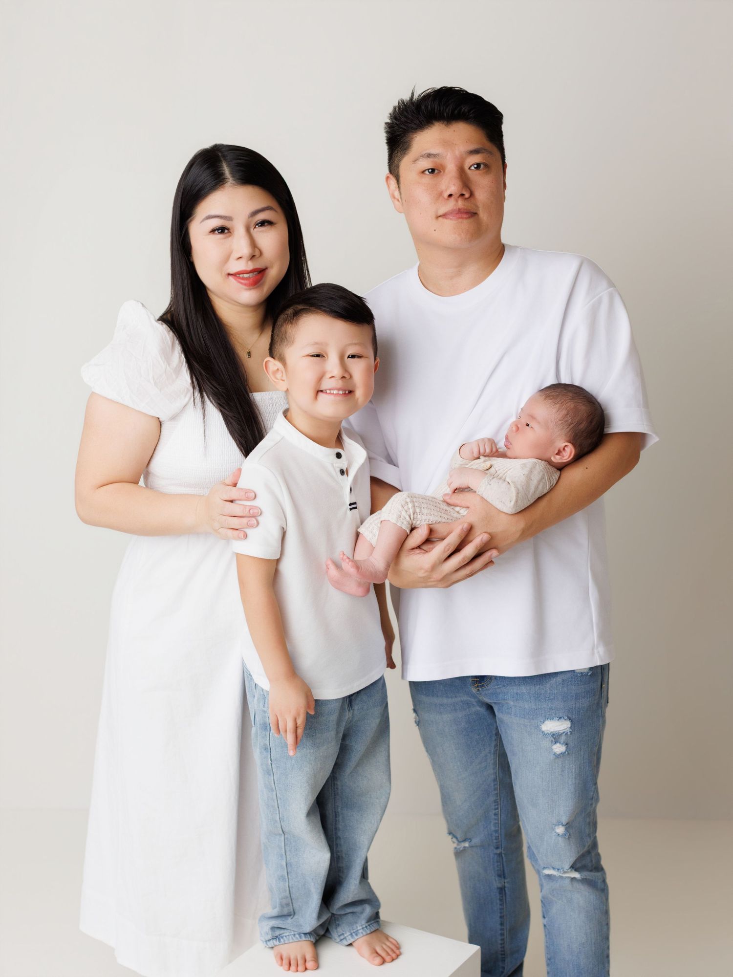 Family in matching white shirts and jeans pose together against neutral backdrop for minimalist studio portraits.