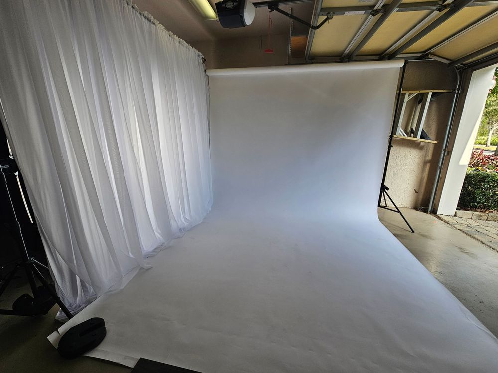 Professional photo studio setup with white backdrop and lighting equipment in a spacious garage-style space.