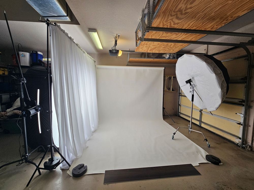 Professional photography studio setup with white backdrop, lighting equipment and wooden ceiling beams visible.