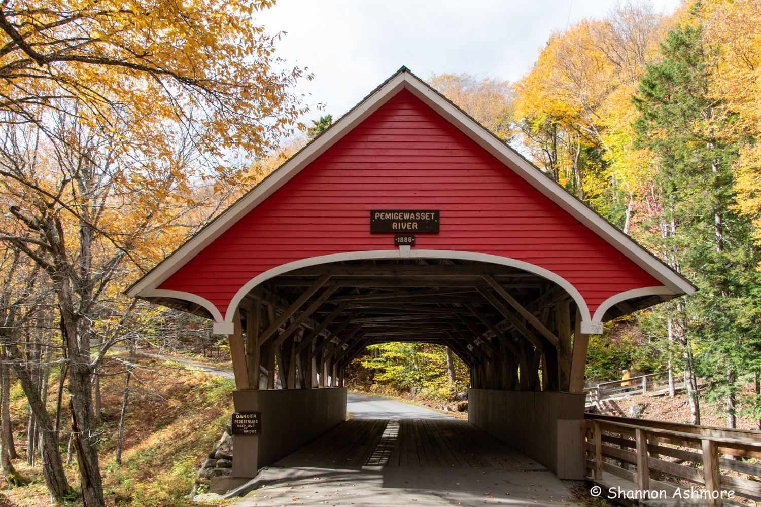 A classic red covered bridge named Pemigewasset surrounded by golden fall foliage in New Hampshire.