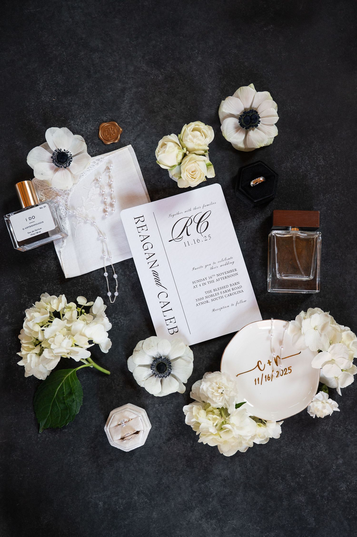 Wedding invitation suite with white flowers and perfume bottles on dark background.