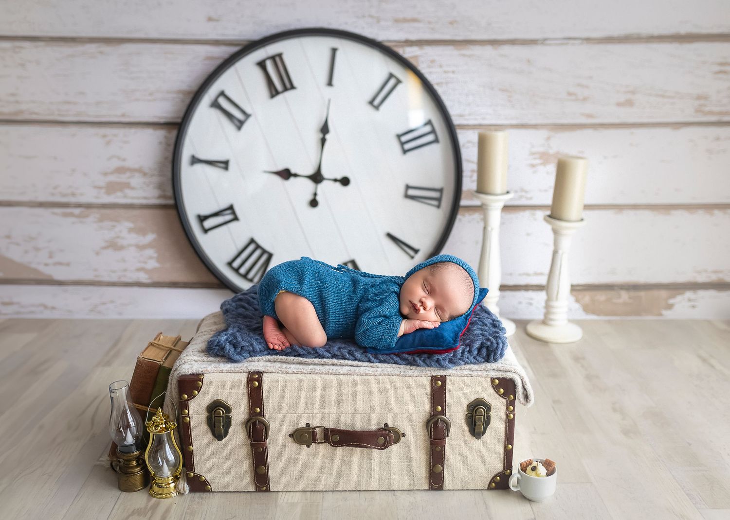 bebe acostado encima de una maleta durmiendo hay un reloj atras grande