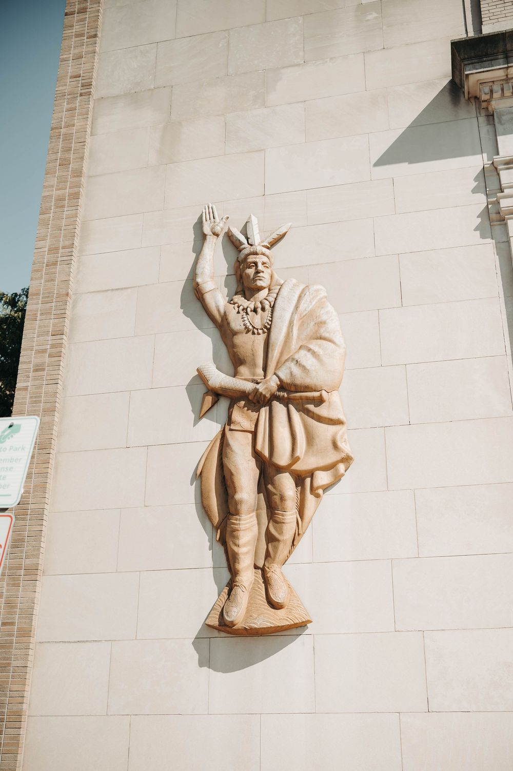 Decorative Native American figure relief sculpture mounted on a beige stone building exterior wall.