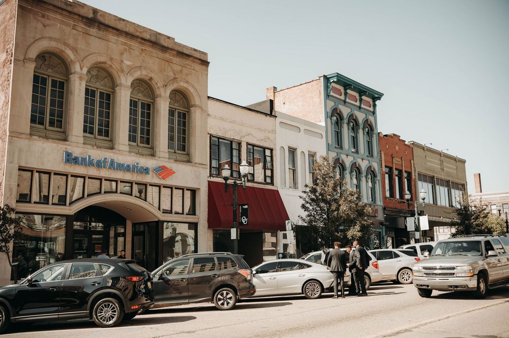 Historic downtown street with Bank of America and colorful storefronts, cars parked along busy sidewalk.