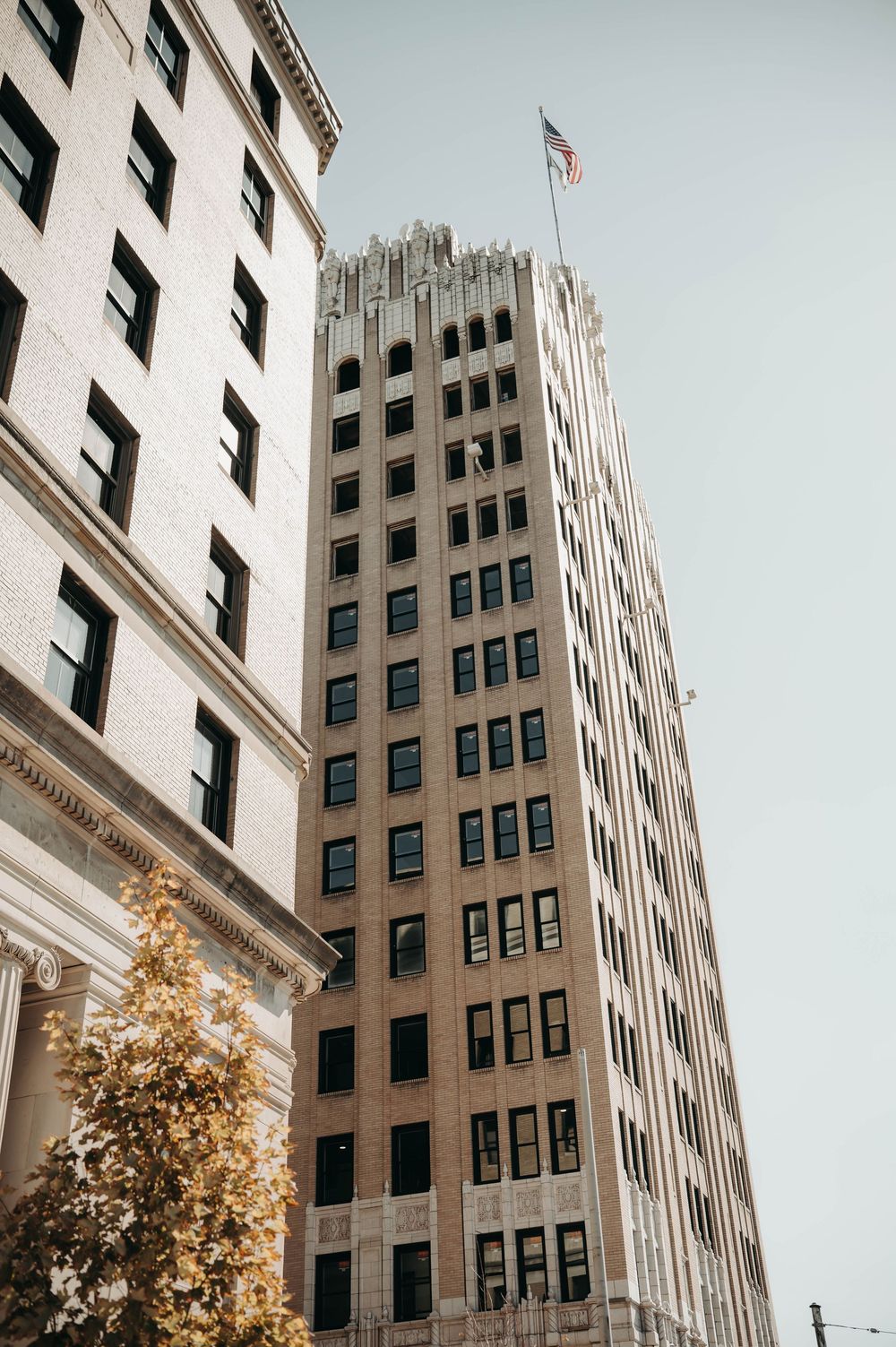 Tall Art Deco skyscraper with American flag on top against clear sky in urban setting.