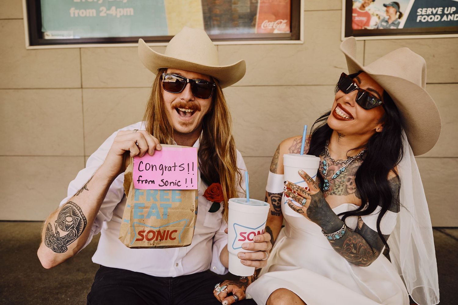 Couple sharing Sonic drinks and showing wedding rings in a casual outdoor setting.