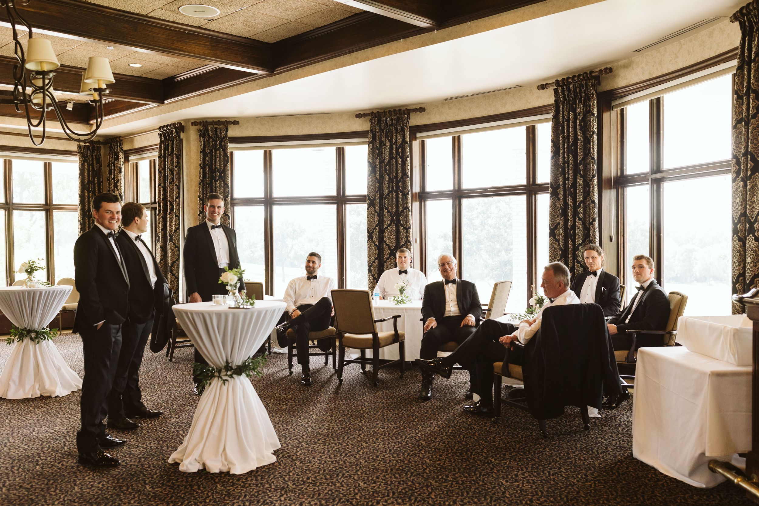Wedding party gathering in an elegant room with large windows and cocktail tables.