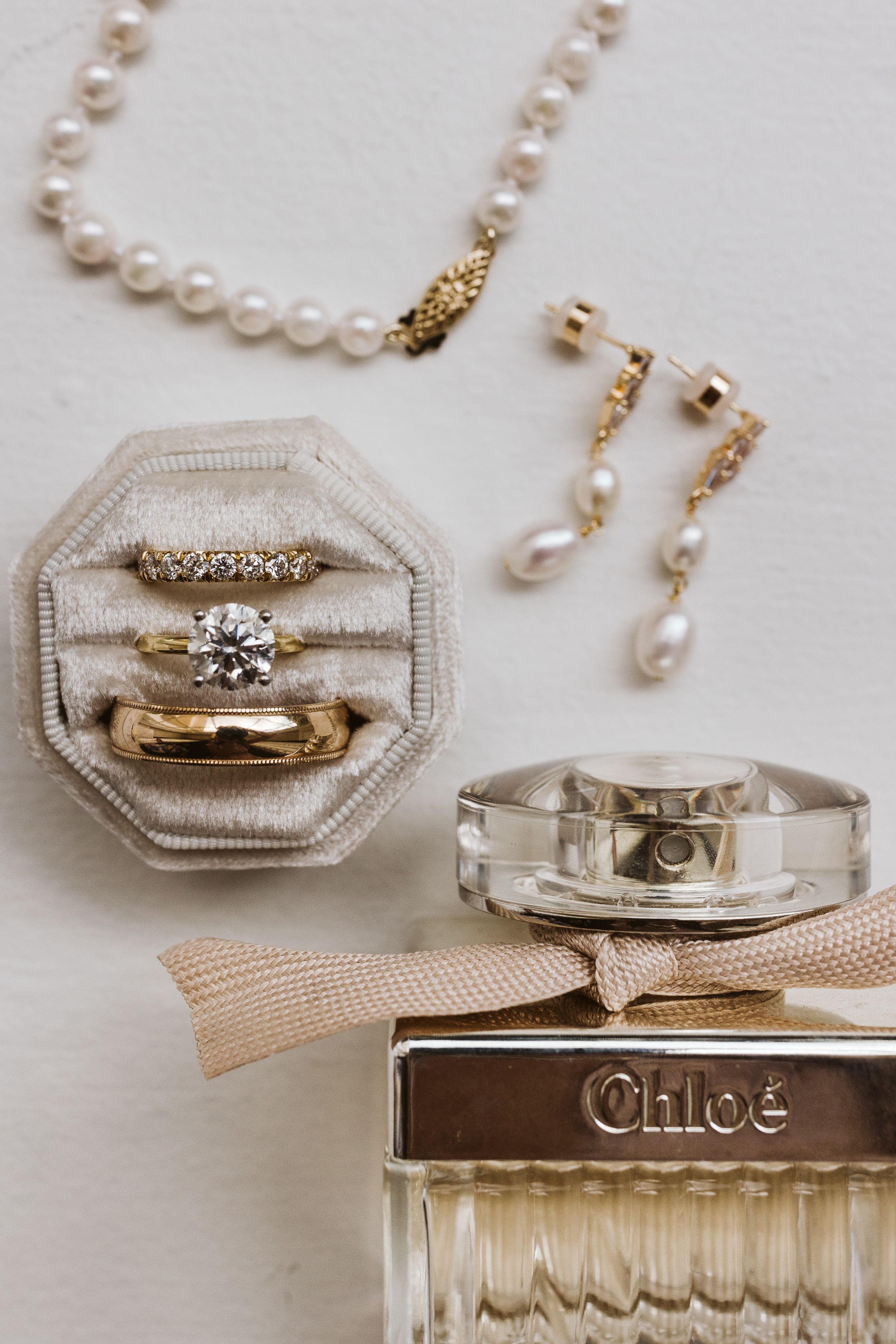 Wedding rings and pearls arranged with a perfume bottle in an elegant display.