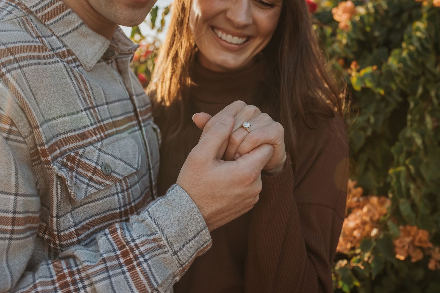 A couple shares a joyful moment while looking at an engagement ring outdoors during golden hour lighting at Windansea Beach.