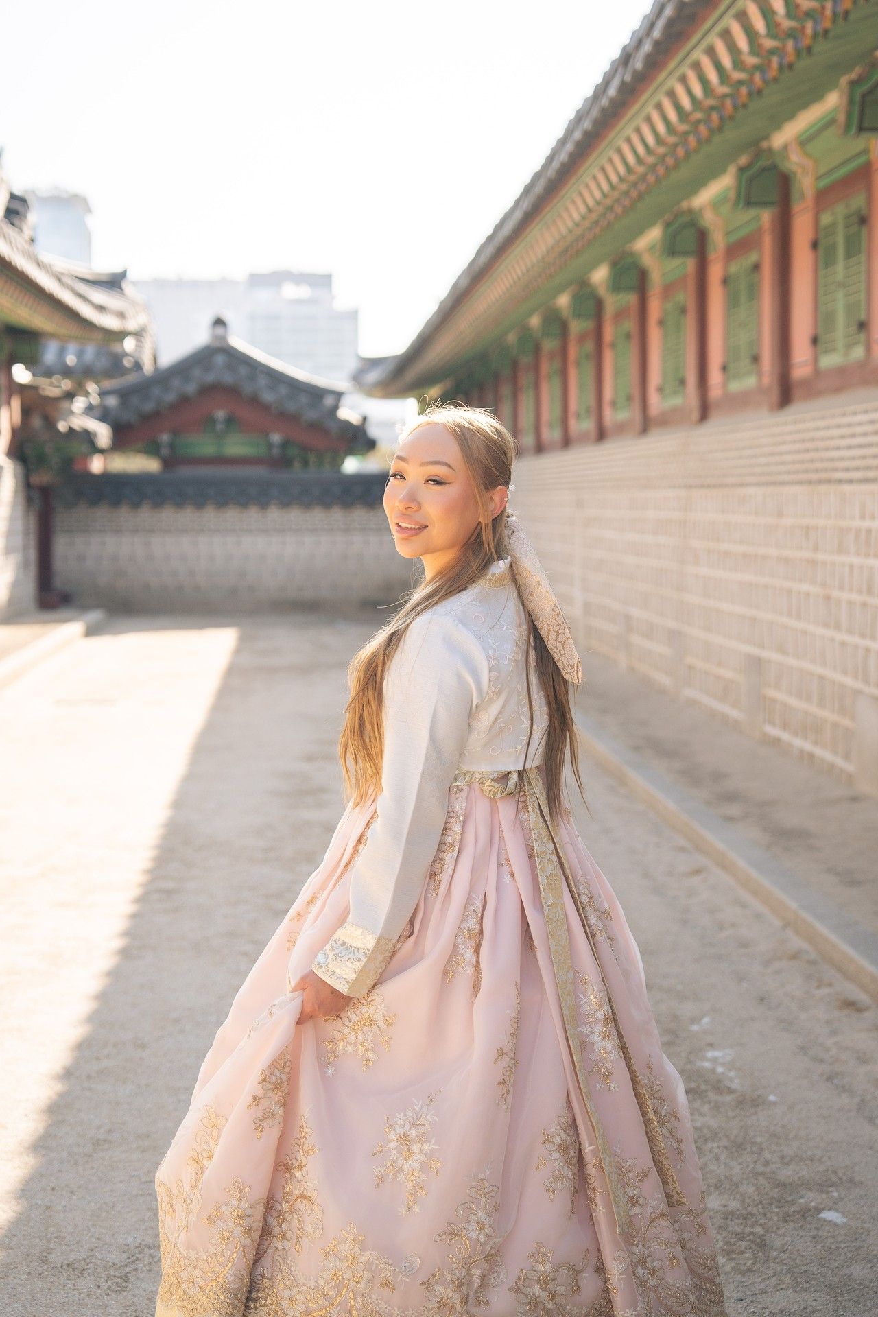 Traditional Korean hanbok dress worn at historic palace courtyard with traditional architecture in sunlit setting.