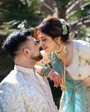 A couple in traditional Indian wedding attire share an intimate moment outdoors in soft natural lighting.
