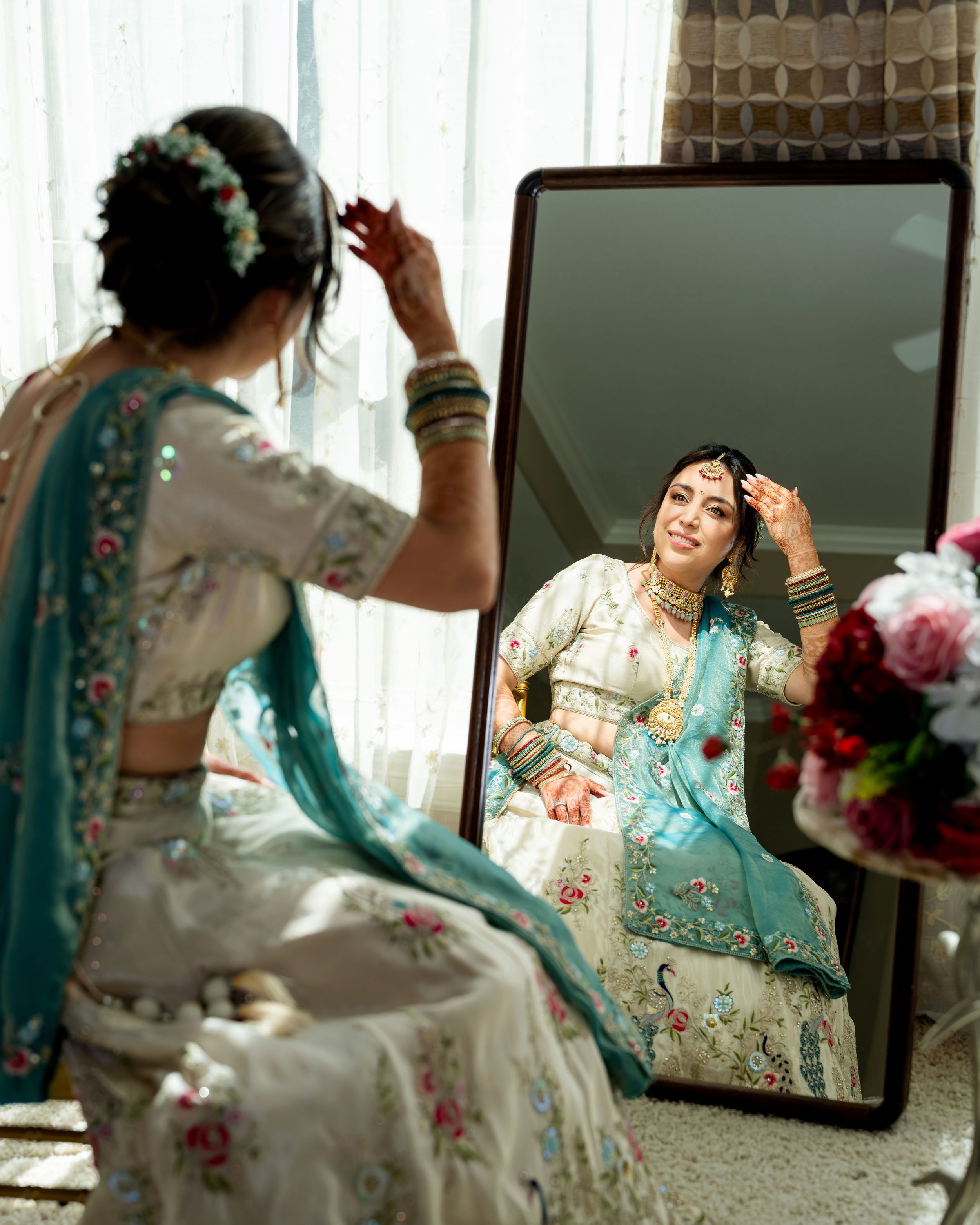 Multiple mirror reflections show someone in an ornate turquoise and cream traditional dress during a photoshoot.