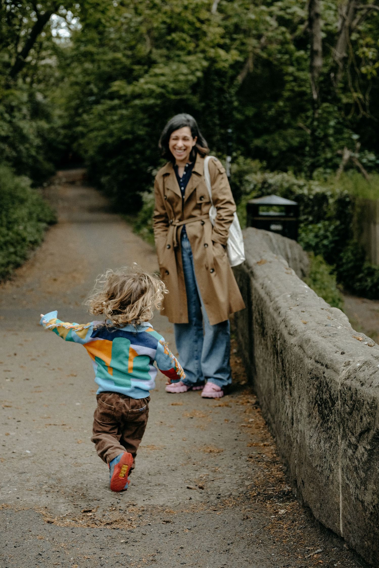 A mother and young child walking along a stone path surrounded by lush greenery, captured during a relaxed outdoor lifestyle family session.