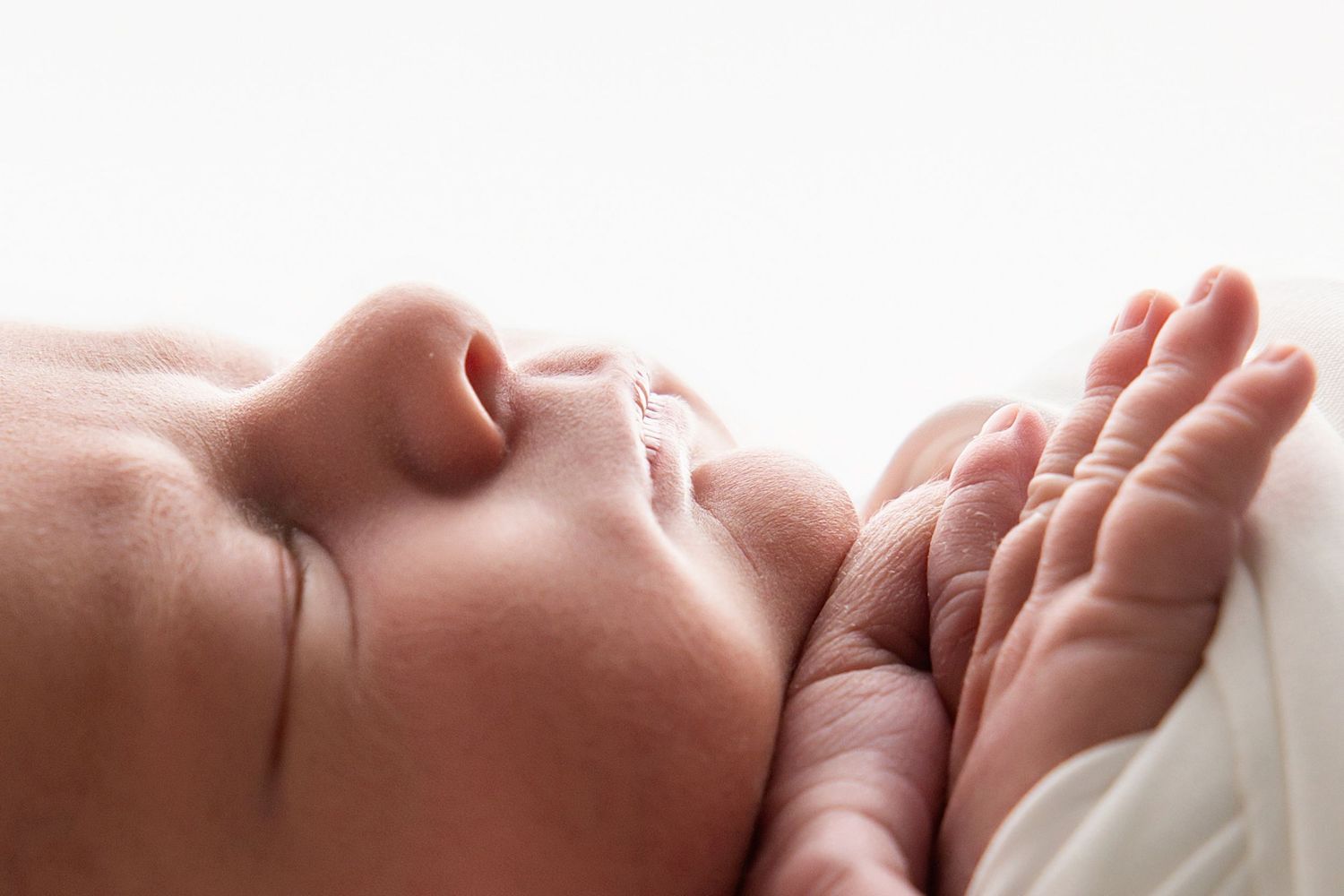 Close-up view of a sleeping newborn baby's face against white bedding.