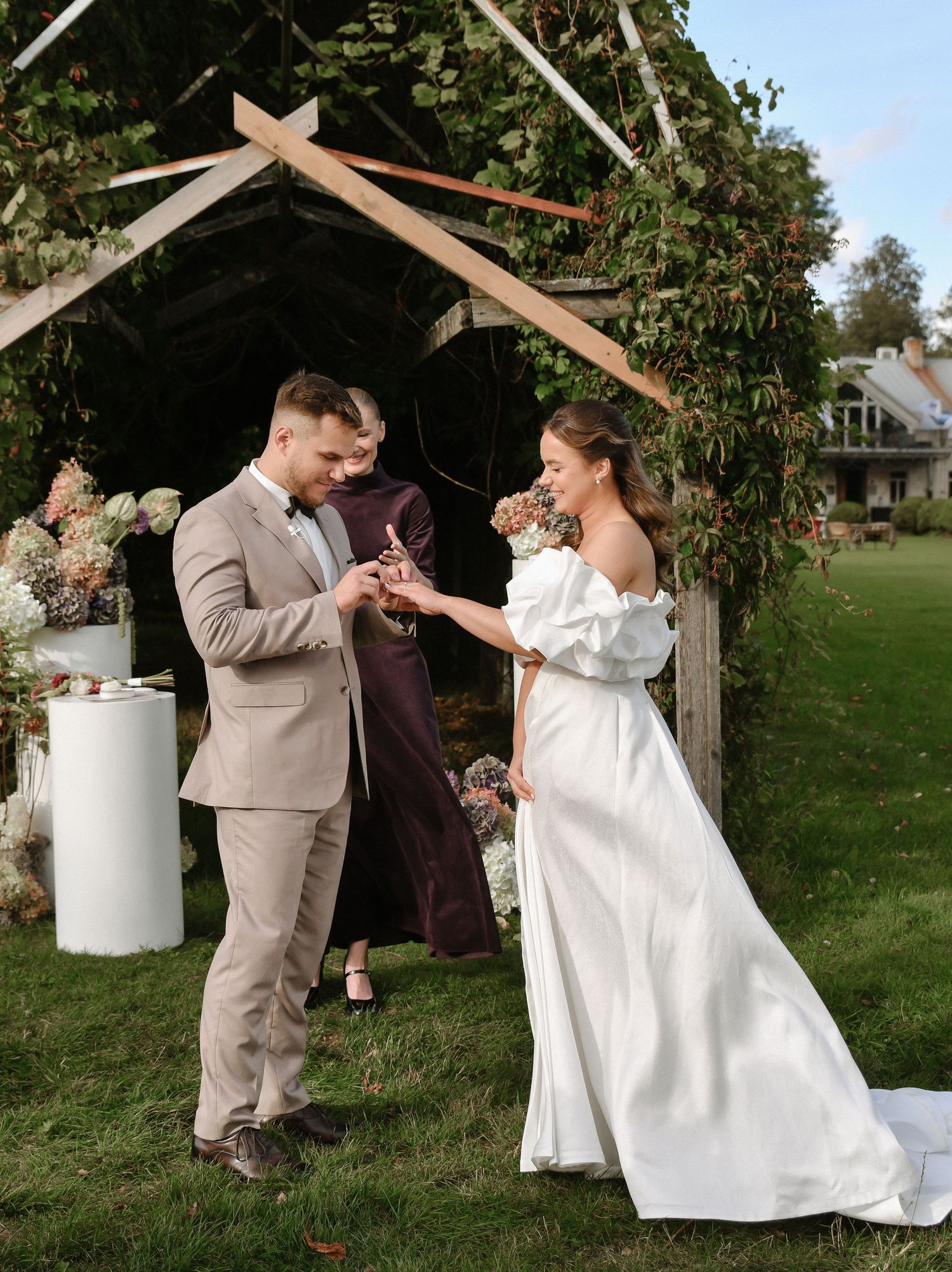 A couple dances playfully under a rustic wooden arch in an outdoor garden setting.