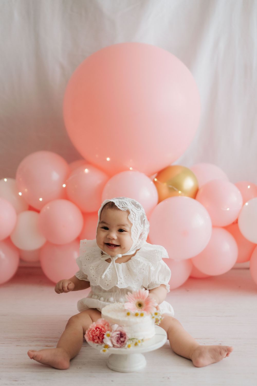 A cake smash photo session setup with pink balloons and a white cake against a light backdrop.
