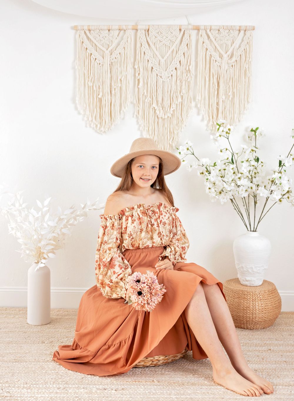 Rustic styled photoshoot featuring terracotta dress and floral arrangements against macrame wall art.