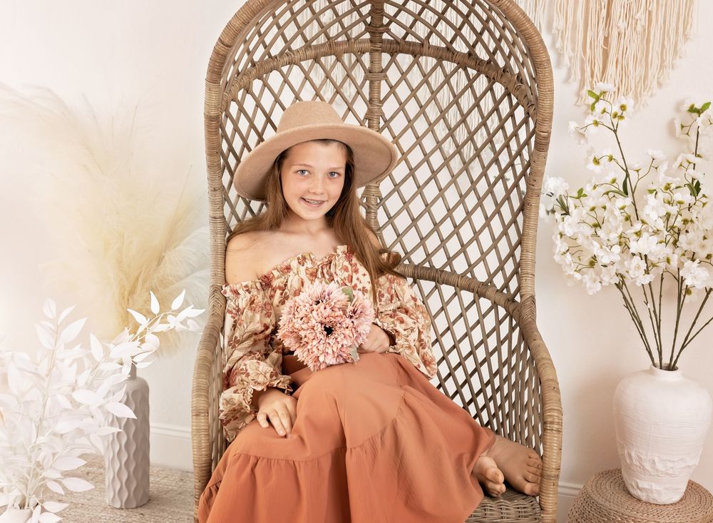 Dreamy boho studio setup with wicker peacock chair and floral decorations in soft pink and cream tones.