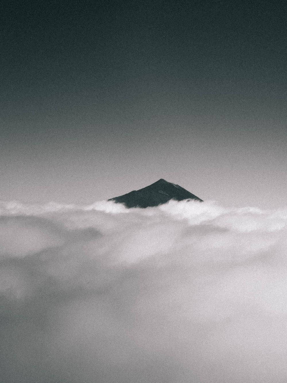 A dramatic black and white panoramic view of Mount Fuji emerging through misty clouds in Japan.