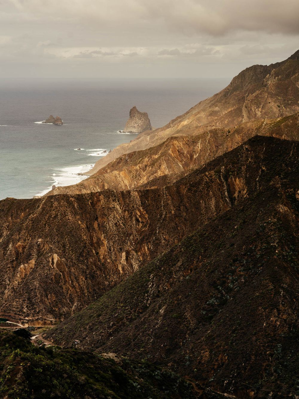 Dramatic coastal cliffs and rock formations along Big Sur's rugged Pacific coastline at sunset with moody overcast skies.