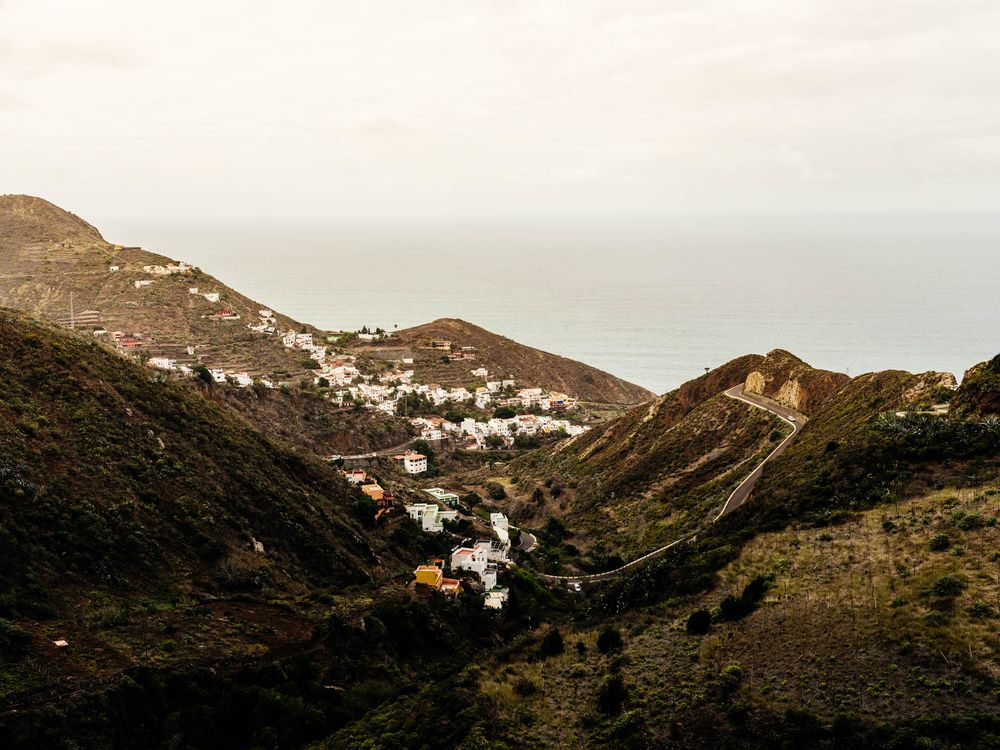 Hillside village with white buildings nestled in mountainous terrain overlooking the Mediterranean Sea at dusk.
