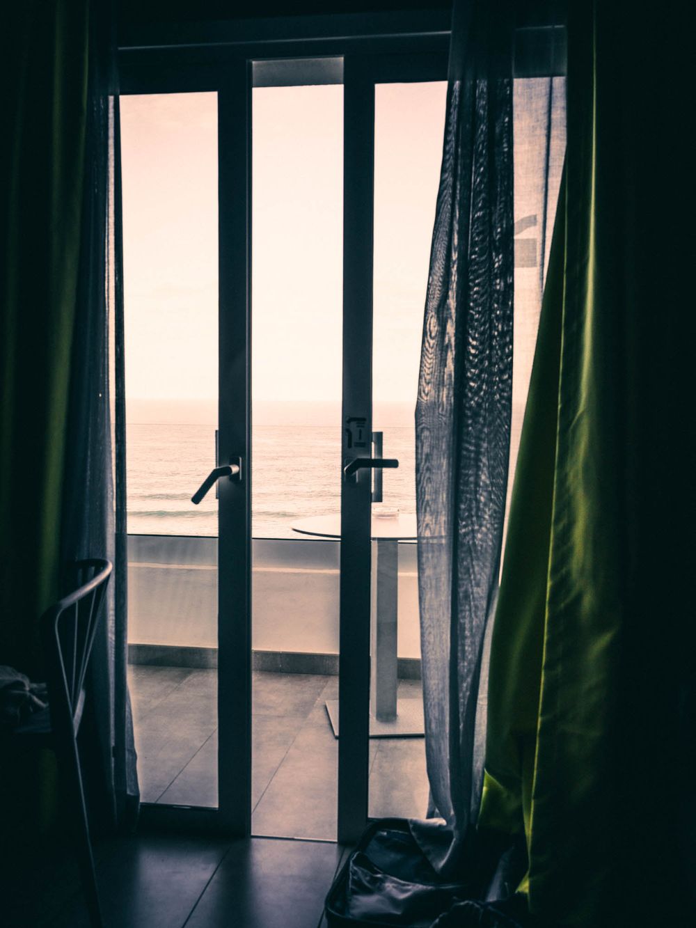 Dark curtains frame a window in a dimly lit room creating a moody, atmospheric interior scene.